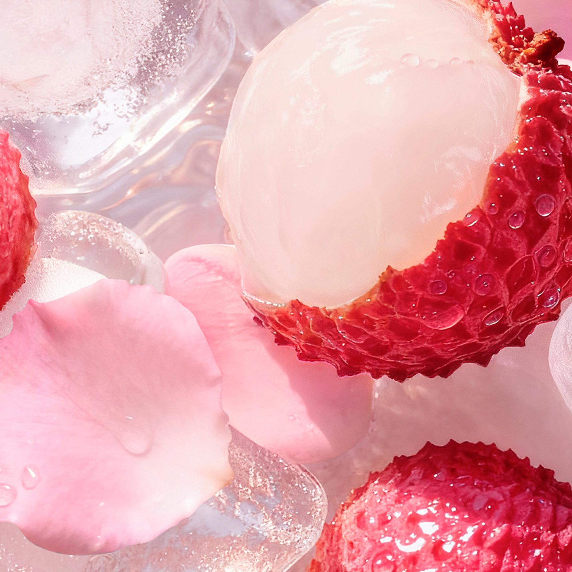 Lychees and rose petals in a cooler filled with ice cubes. Next to it a pink paddle and a striped pink towel on a sandy background.