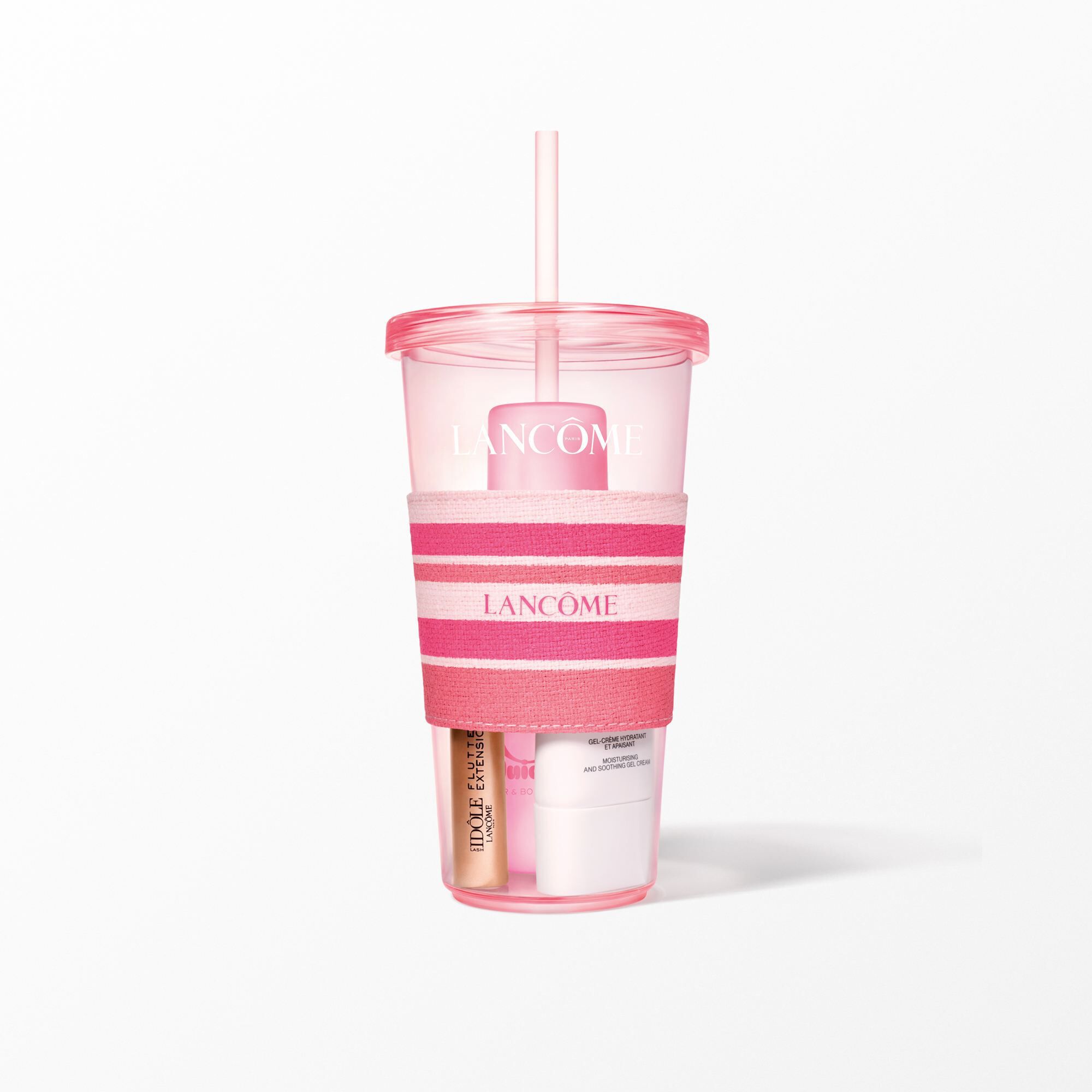A close-up of the pink Lancome tumbler with a pink and white striped sleeve holding beauty products.