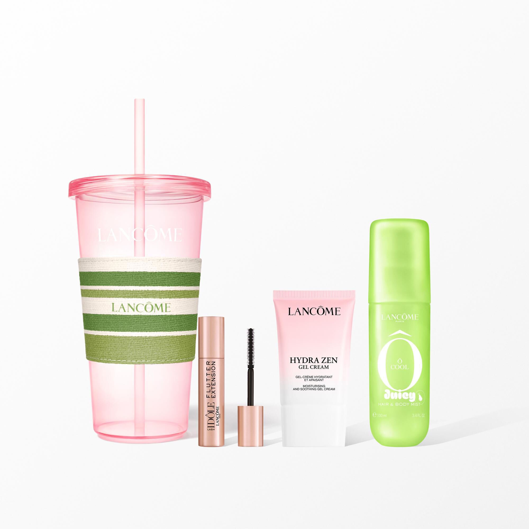 A Lancome beauty set featuring a pink reusable tumbler with a striped sleeve, mascara, face cream, and a green hair and body mist.