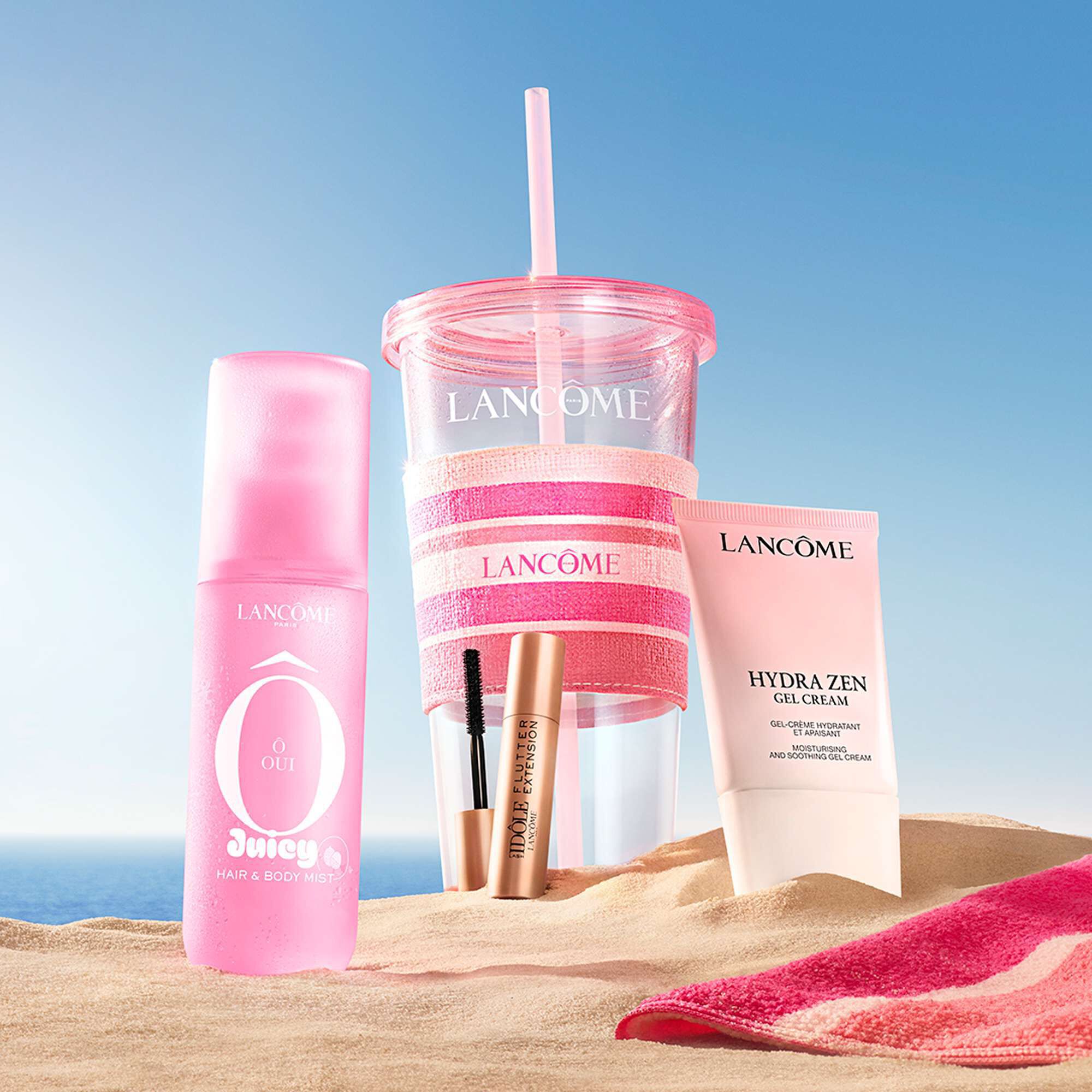 A lifestyle shot of the Lancome beauty set displayed on a sandy beach under a blue sky.