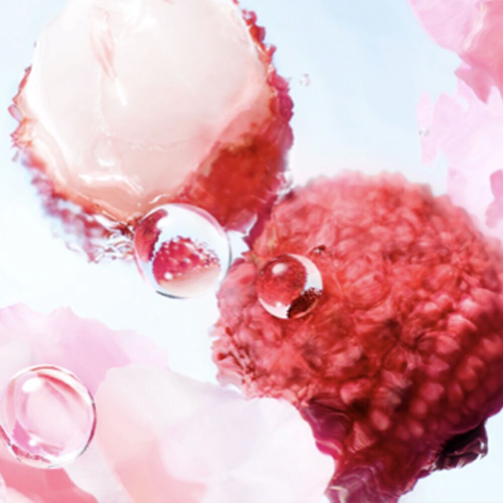 [ingredients visual] Close-up image of lychees and rose flower petals in water, surronded by water droplets on a light blue background, with soft, diffused lighting.
