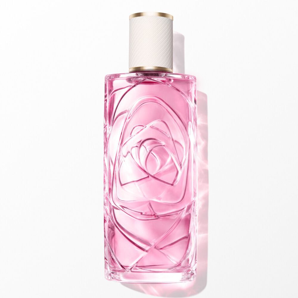 A transparent glass perfume bottle with light pink liquid, textured design, and white and gold cap. Centered vertically on a white background with soft, bright front lighting and a subtle shadow.